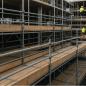 Rows of timber planked scaffold platforms with guardrails, workers in high-visibility vests on the decks above